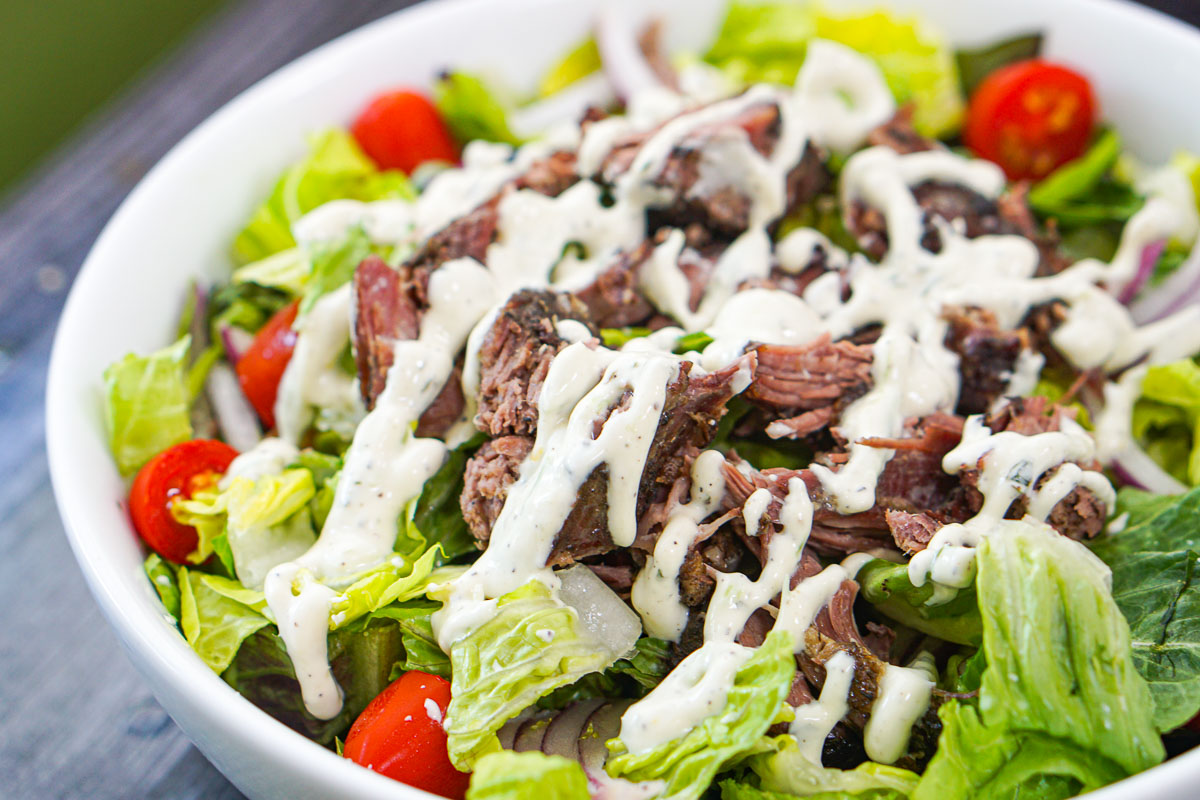 closeup of a bowl of salad topped with greek lamb and tzatziki dressing