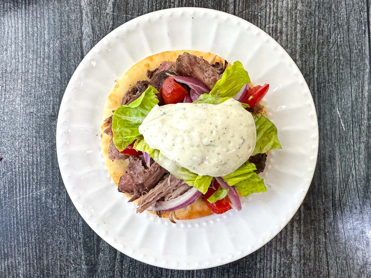 white plate with a open faced gyro topped with yogurt dressing