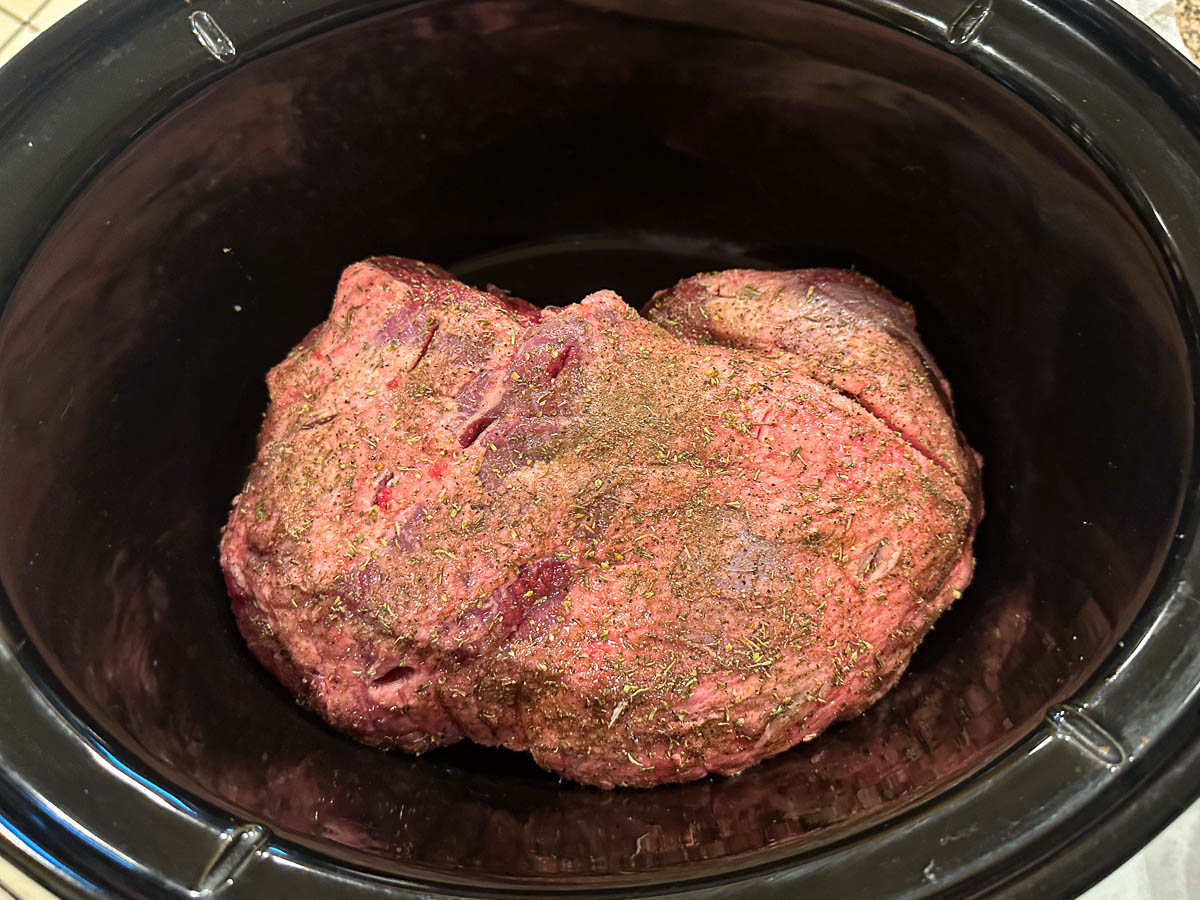 crock with raw leg of lamb with spices all over it