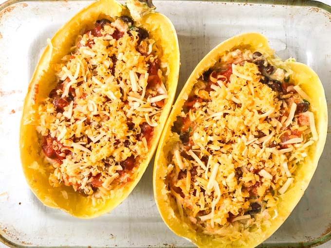 baking dish with 2 halves of spaghetti squash stuffed with Mexican casserole and topped with cheese before baking