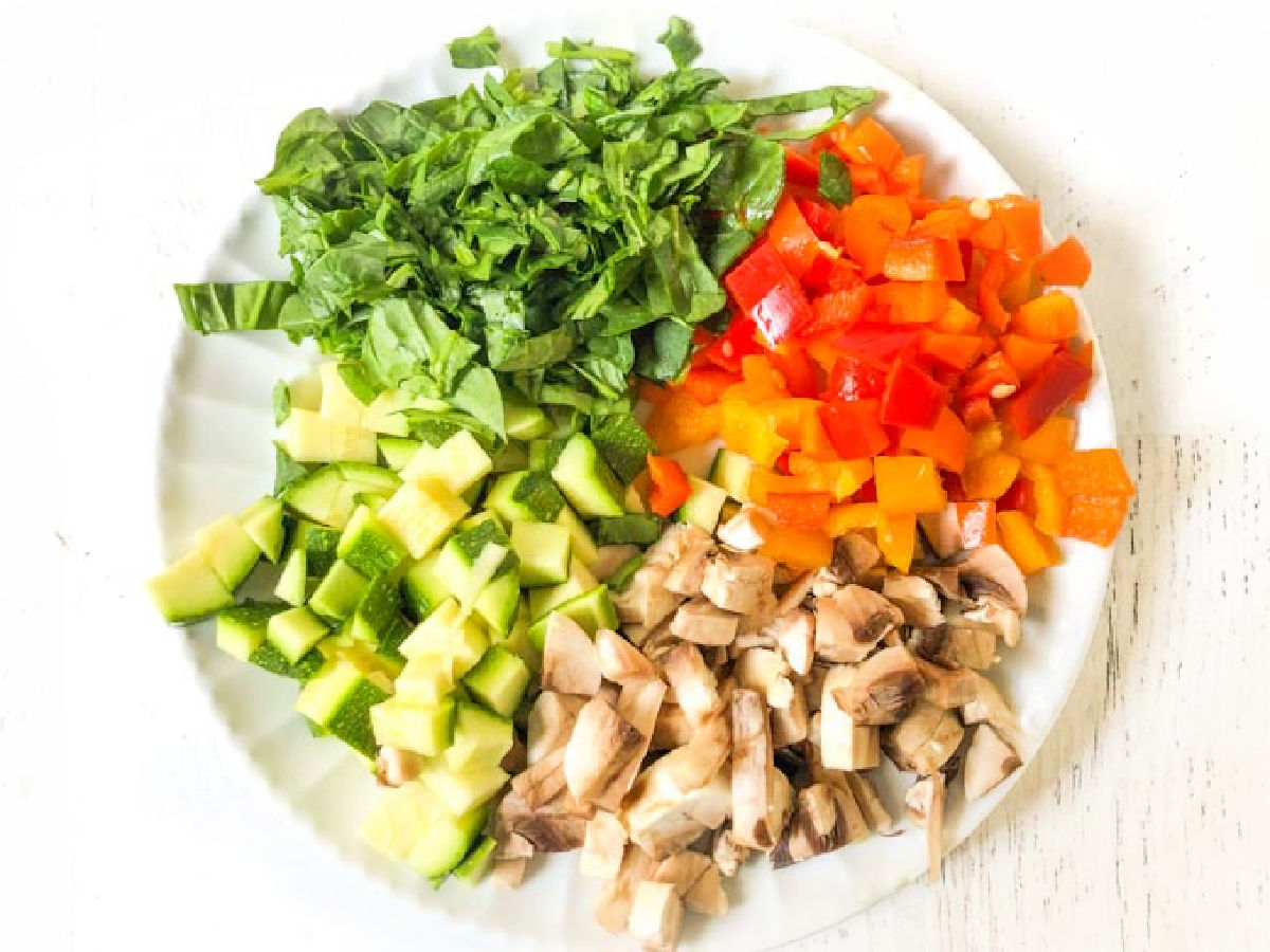 Plate with chopped veggies - spinach, peppers, zucchini and mushrooms.