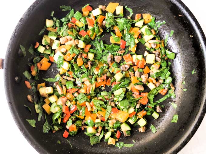 skillet with cooked veggies with spinach