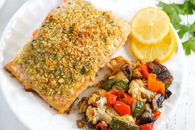 closeup of a piece of crusted salmon, roasted veggies and lemon slices