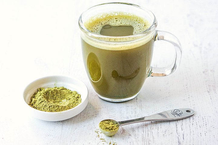 a cup of matcha green tea and white dish and silver scoop with matcha powder