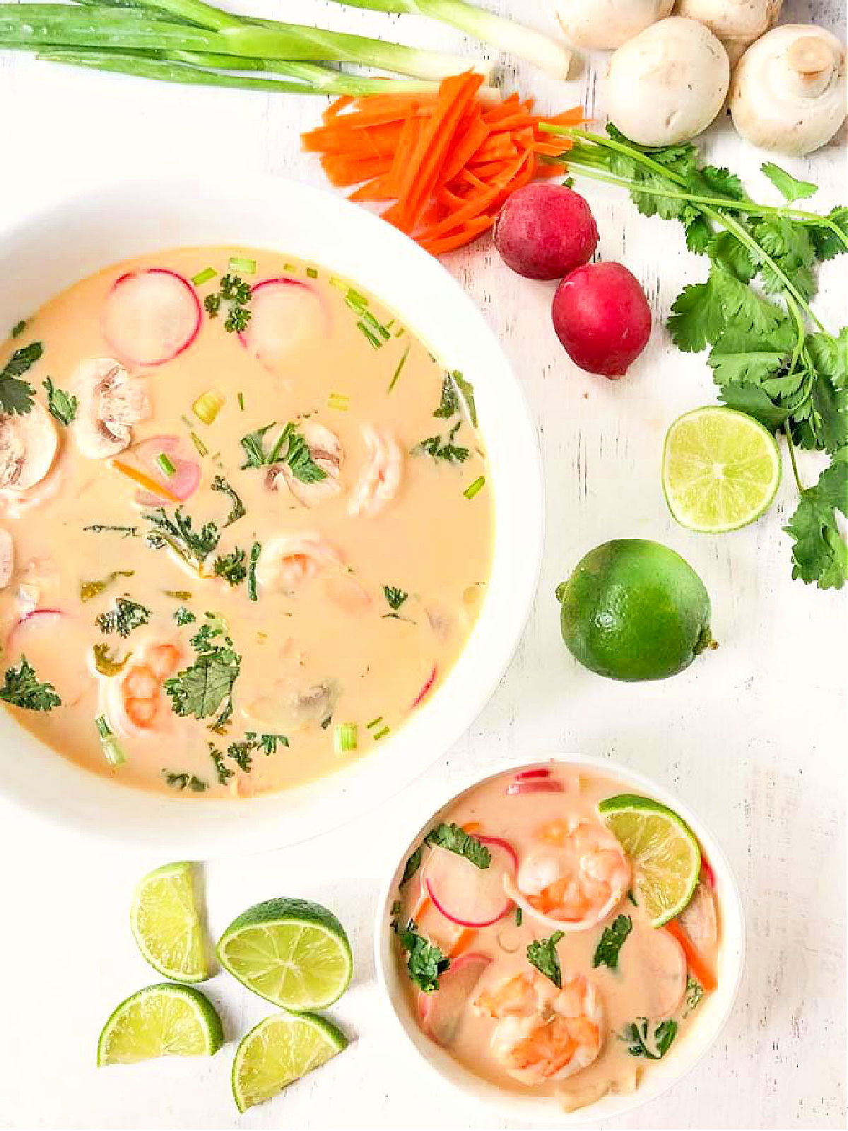 Aerial view of white bowls with keto shrimp Thai curry soup and fresh veggies surrounding.