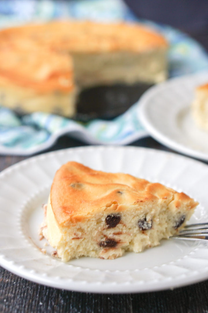 closeup of a white plate with a slice of keto chocolate chip cheesecake with the rest of the cake in the background