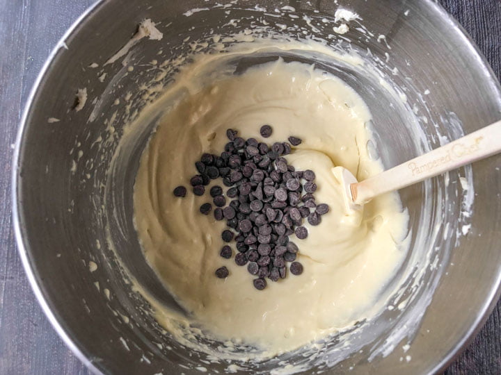 silver mixing bowl with cheesecake batter, with chocolate chips and white spatula