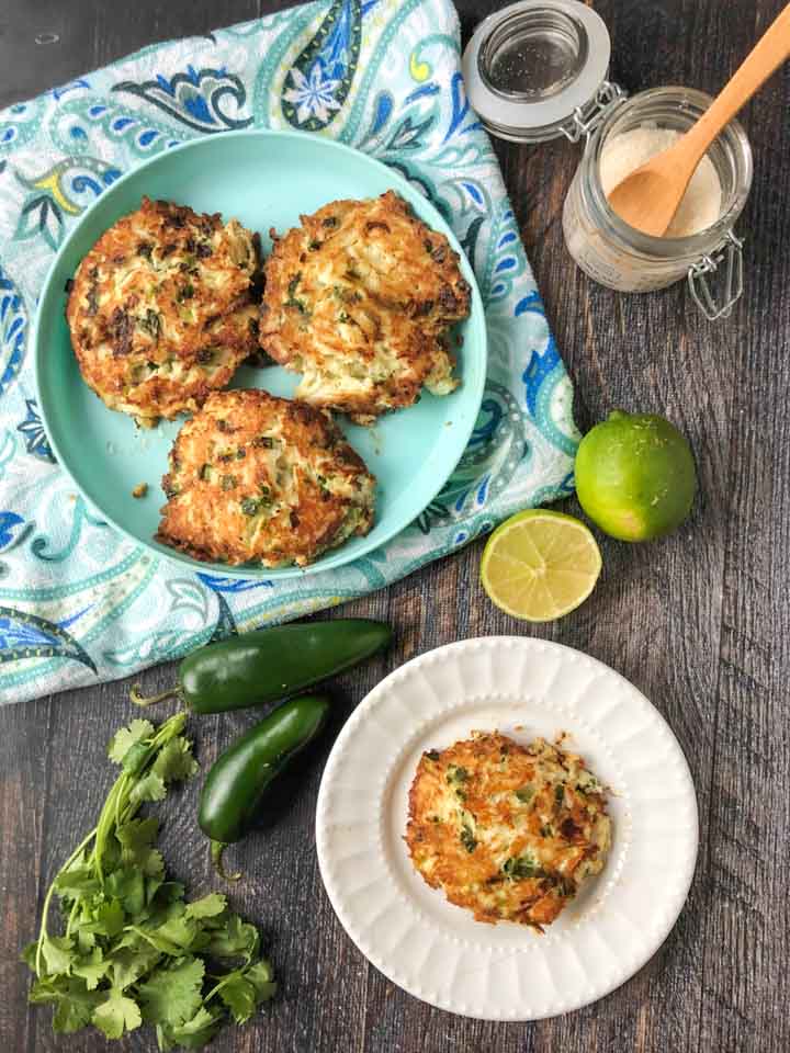 3 low carb crab cakes on aqua plate with blue paisley tea towel underneath and fresh  jalapenos, limes and cilantro