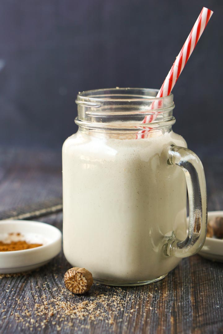 glass jar with low carb eggnog shake with a red and white striped straw and grated whole nutmeg