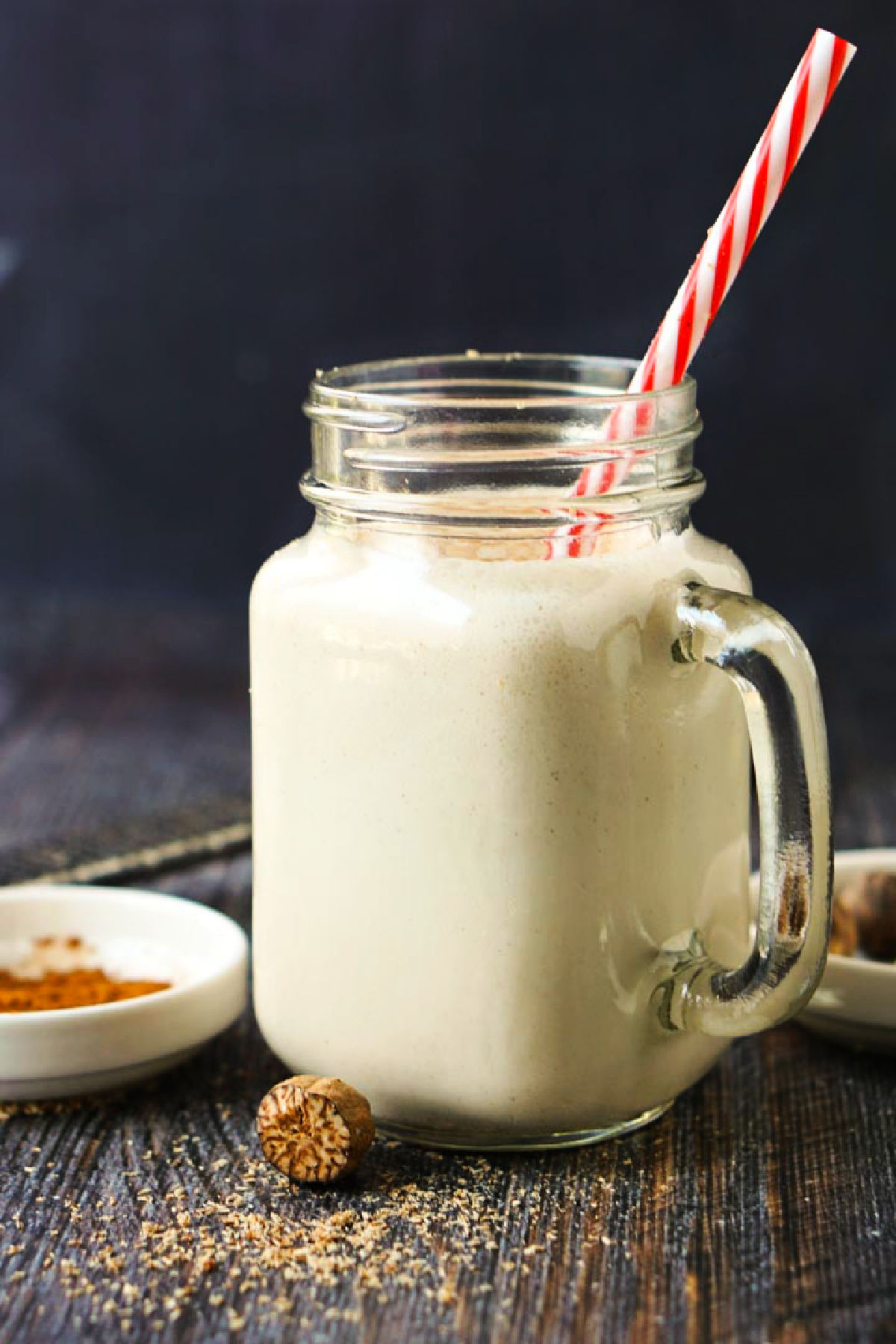 A glass mug with the finished keto eggnog smoothie with fresh grated nutmeg scattered on the table.
