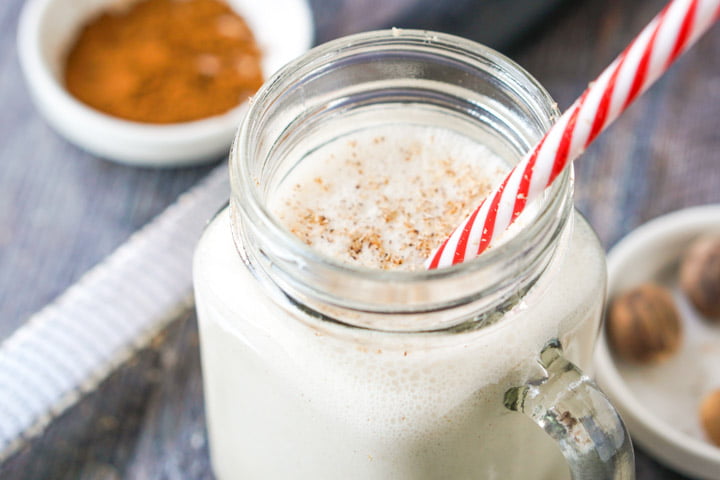 closeup of a glass jar with low carb eggnog shake with a red and white striped straw