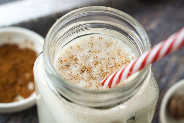 closeup of a glass jar with eggnog shake with a red and white striped straw