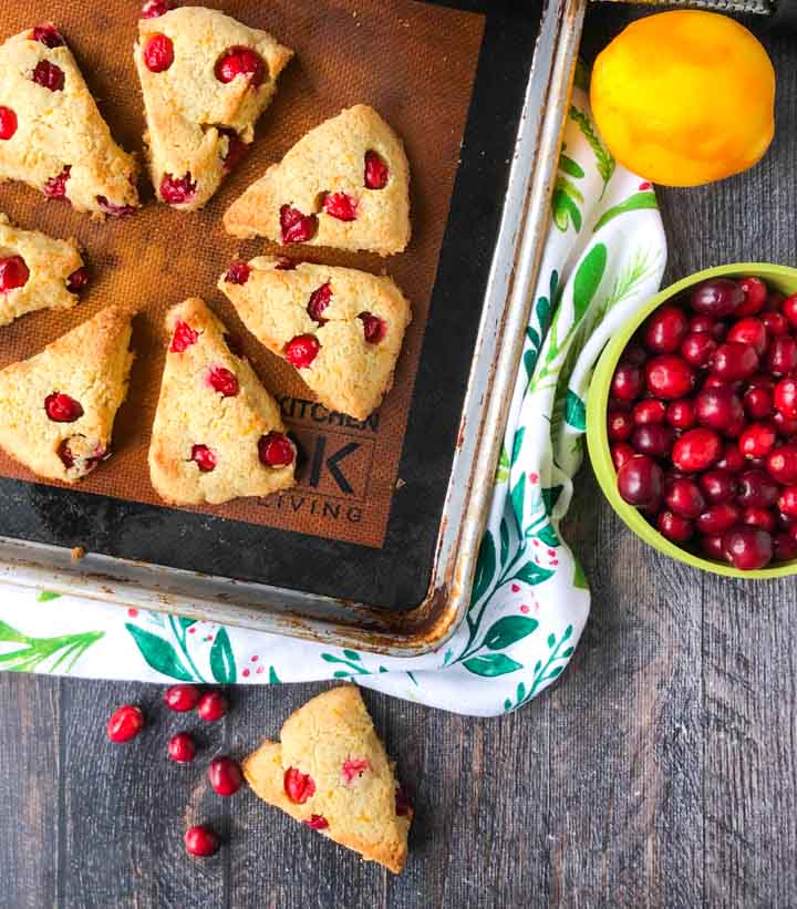 cookie sheet with keto cranberry orange scones and a bowl of fresh cranberries and an orange