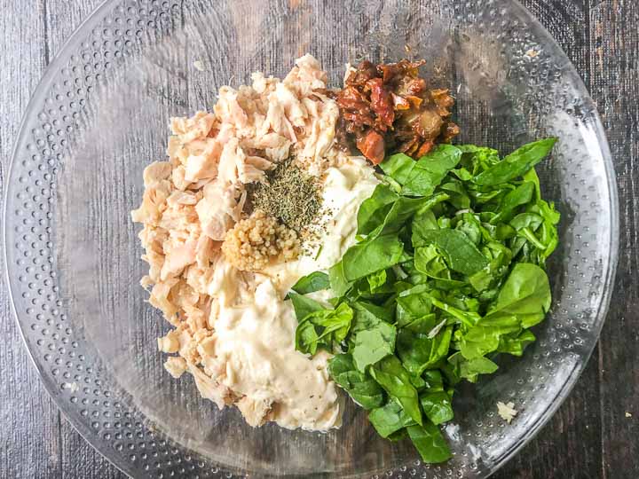 ingredients for hot keto chicken dip in a glass bowl: cream cheese, mayo, spinach, sun dried tomatoes and spices