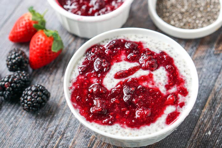 white bowl with low carb chia pudding with a berry sauce and fresh strawberries and blackberries too