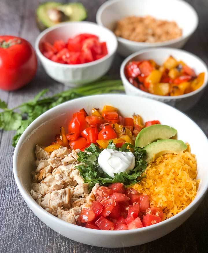 white healthy keto burrito bowl with the toppings in white bowls in the background
