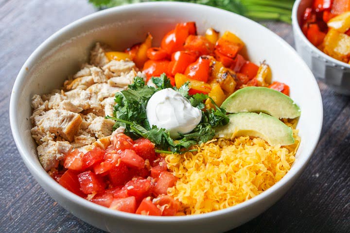 white healthy keto burrito bowl with chicken, tomatoes, cheese, roasted peppers, avocado, cilantro and sour cream