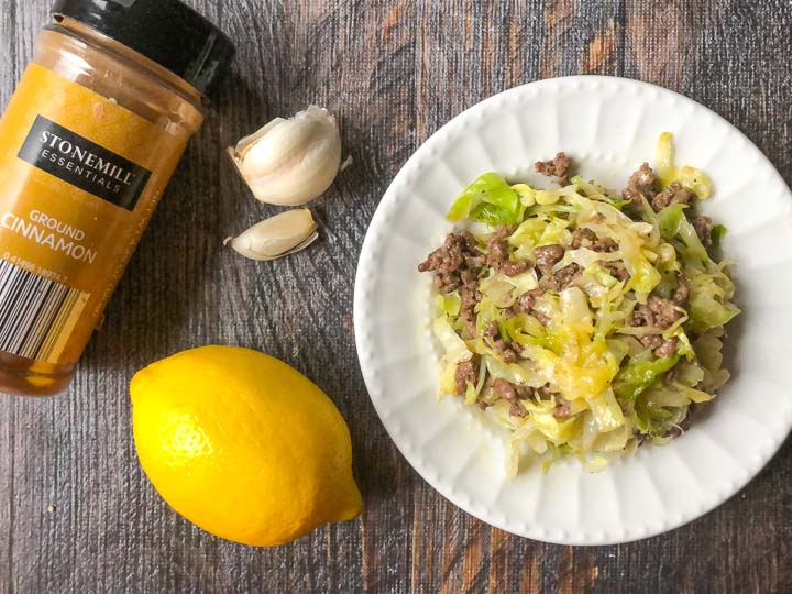 a white plate of Middle Eastern ground beef and cabbage with a lemon, cinnamon and garlic cloves