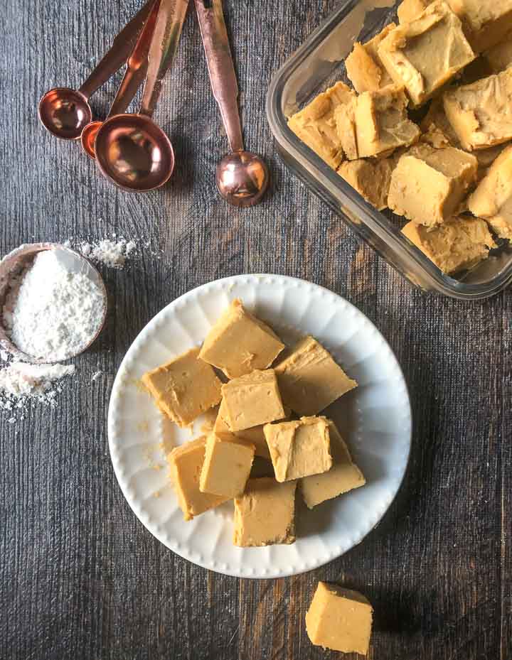 White plate with keto peanut butter fudge pieces with copper measuring spoons and a glass dish with more fudge and a cup of Swerve sweetener