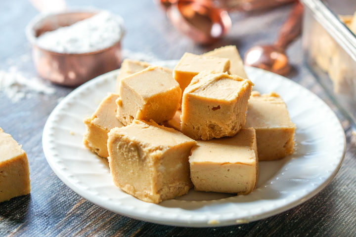 White plate with keto peanut butter fudge pieces with copper measuring spoons in the background