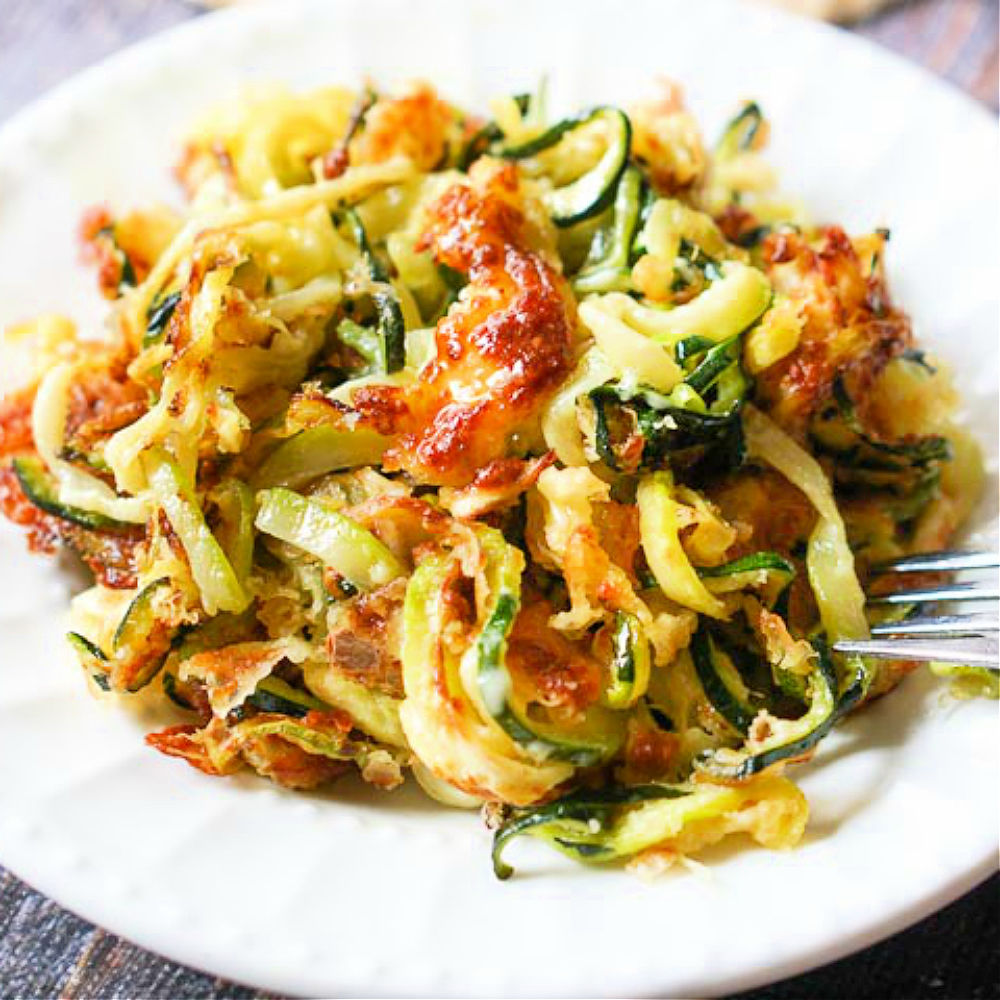 cheesy zucchini noodles from the air fryer on a white plate