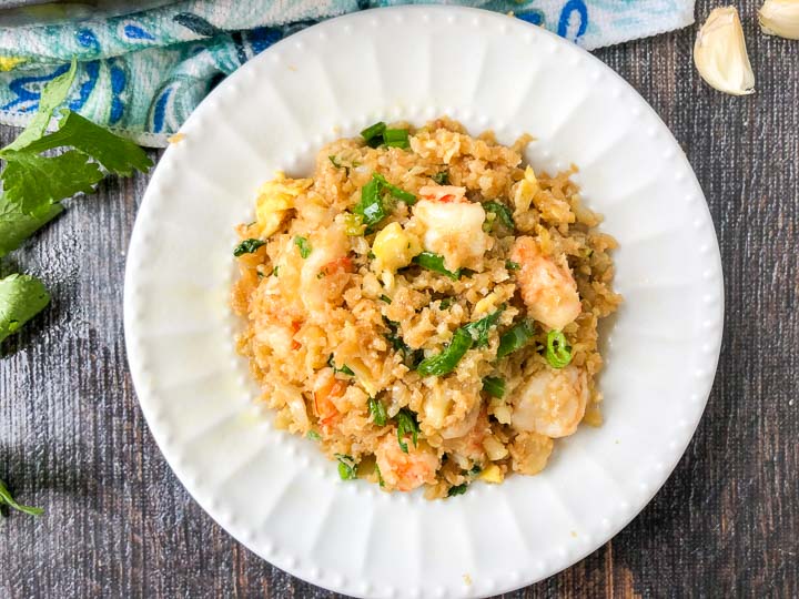 white plate with a serving of cauliflower fried rice with sprigs of parsley and cloves of garlic