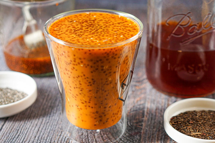 glass with low carb Thai tea chia seed drink with jars of tea and chia seeds in the background