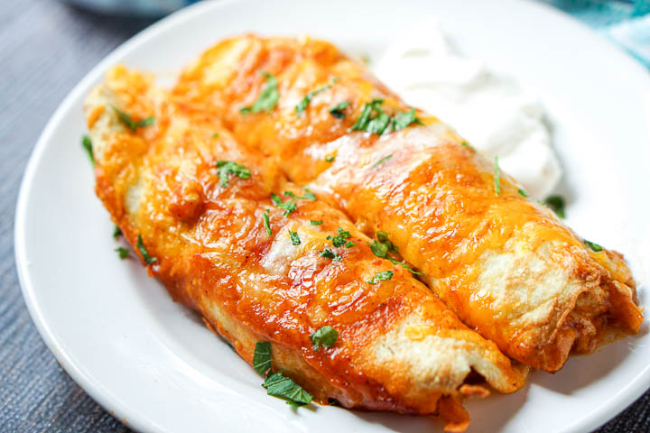 closeup of a white plate with sour cream and two keto chicken enchiladas with cilantro on top