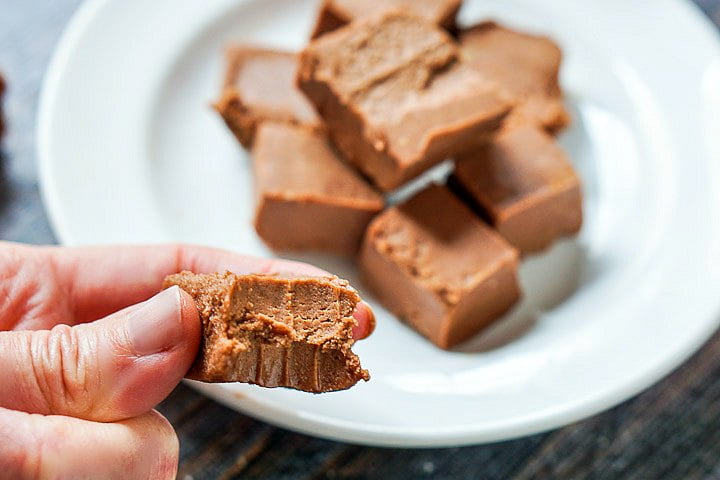 hand holding a piece of low carb fudge with a white plate full in the background