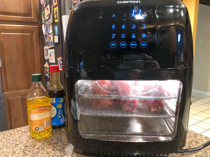a Chefman air fryer with pork kebabs cooking and a bottle of soy and olive oil