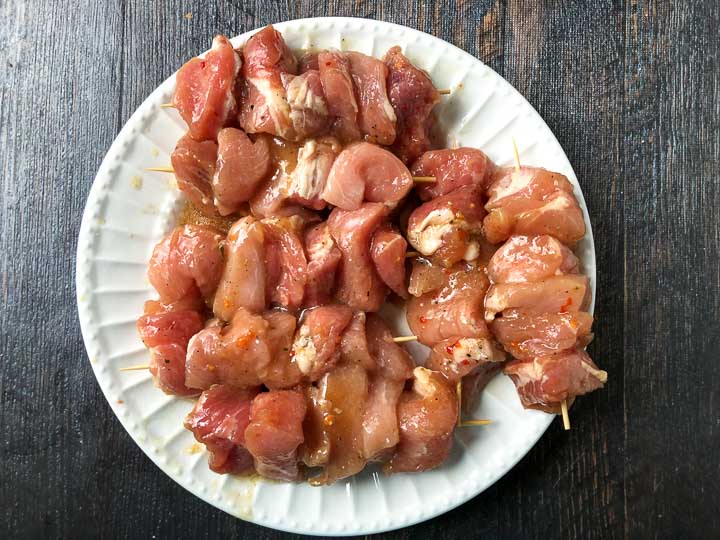 white plate with marinaded raw pork kebabs 