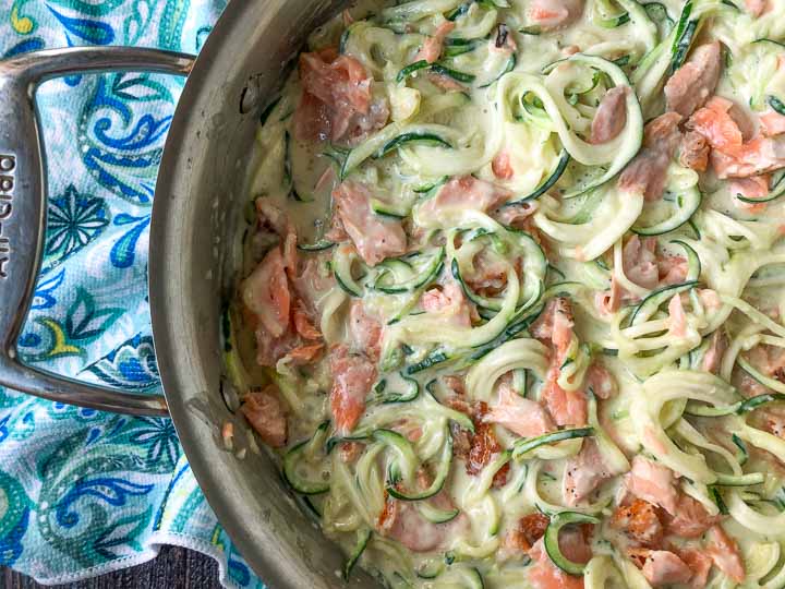 a pan with the keto salmon alfredo with zucchini noodles and a blue paisley tea towel