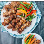 aerial view of white plate with keto pork bites on skewers and julienne vegetables and text