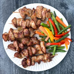 white plate with keto air fryer pork bits on skewers with veggies