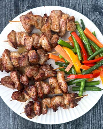 white plate with keto air fryer pork bits on skewers with veggies
