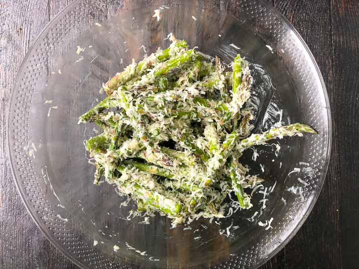clear glass bowl with raw asparagus fries coated in mayo and asiago cheese