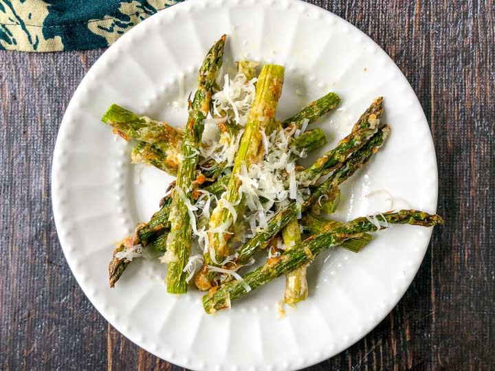 white plate with a few asparagus fries with shredded asiago on top