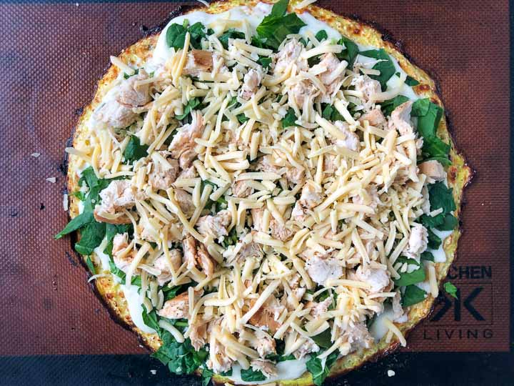 cooked cauliflower crust with all the fixings ready to go back in the oven