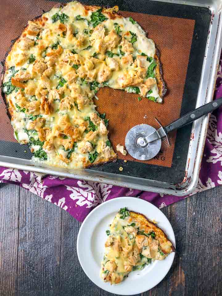 cookie sheet  and white plate with chicken alfredo pizza with a low carb cauliflower crust and a pizza cutter