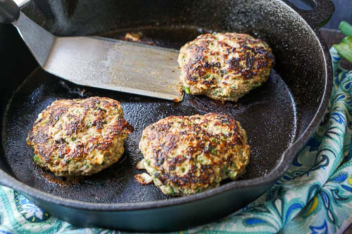 3 keto turkey burgers in a cast iron skillet with a stainless steel spatula