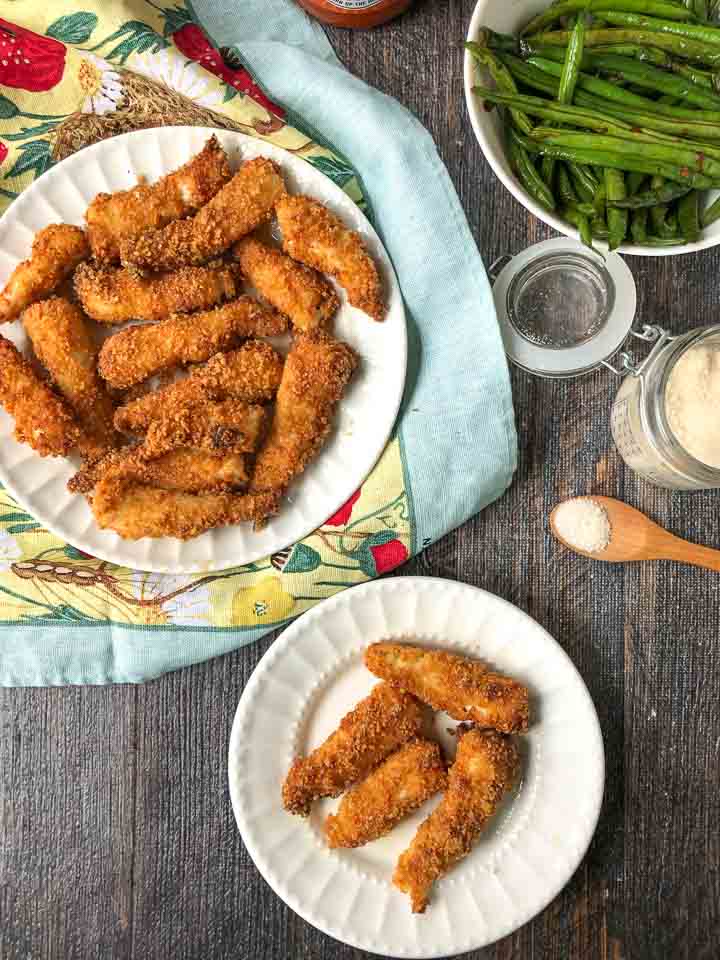 white plates full of keto air fryer fish sticks on a colorful towel and green beans