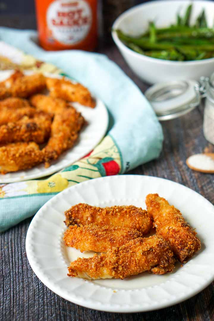 small white plate with air fryer fish sticks and a bowl of green beans in background