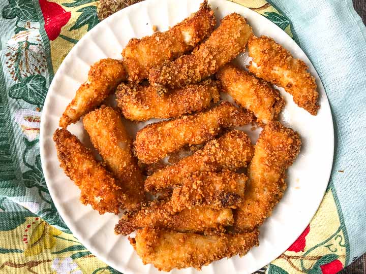 white plate full of gluten free keto fish sticks made in the air fryer and colorful tea towel below it