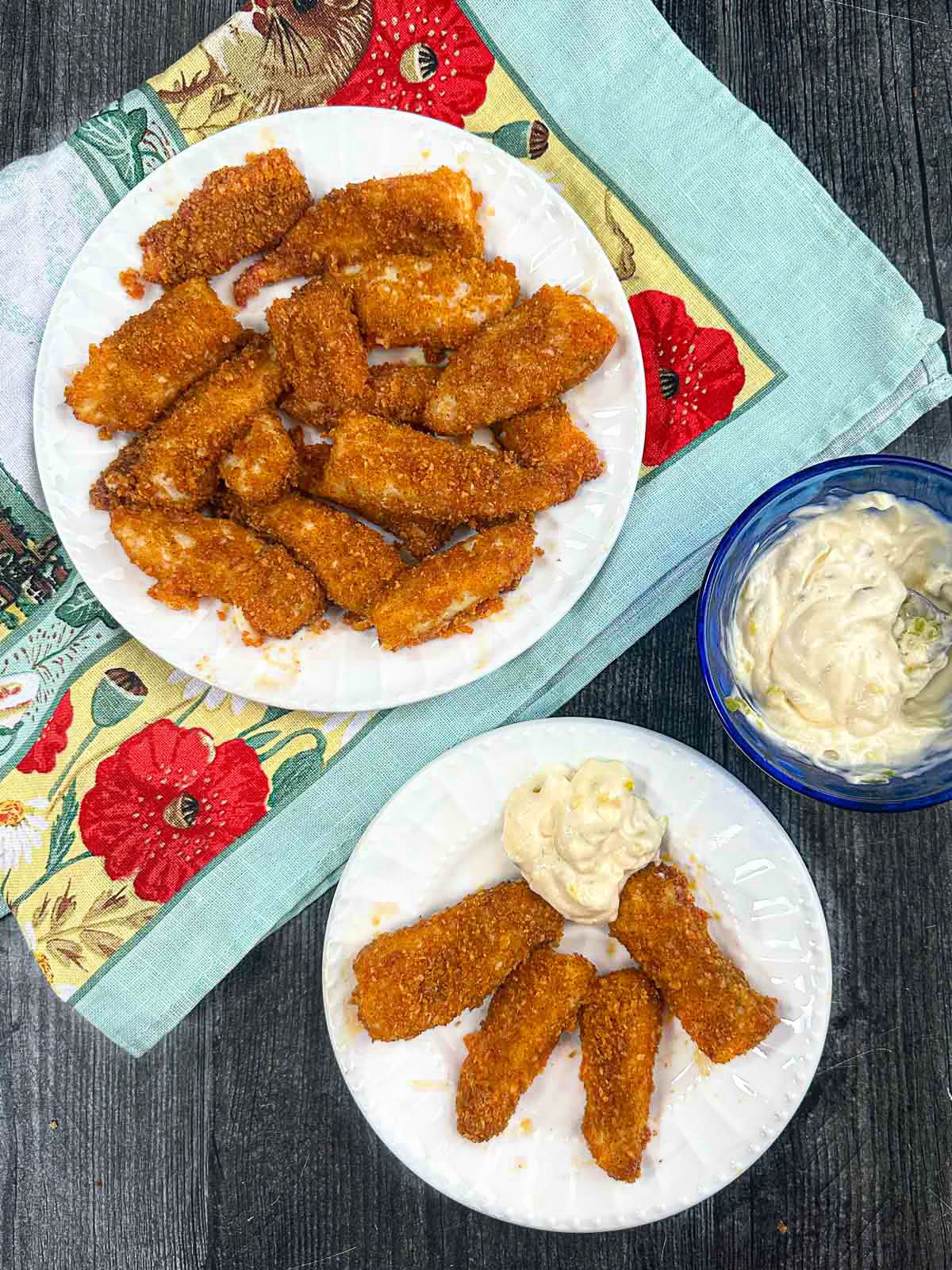 Aerial view of white plates of keto fish sticks made in the air fryer and a bowl of tartar sauce.