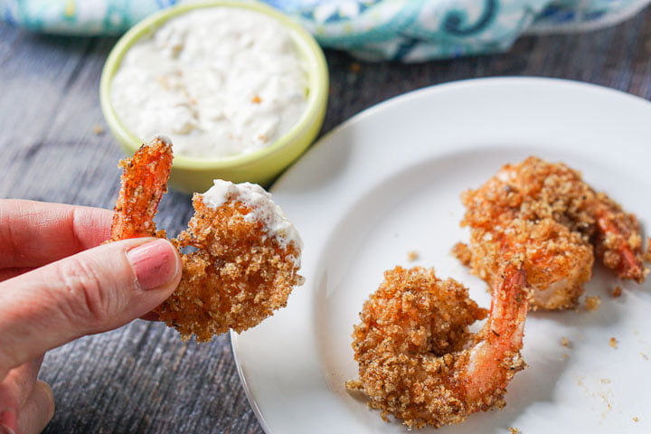 hand holding a fried shrimp that is dipped in homemade tartar sauce which is in the background