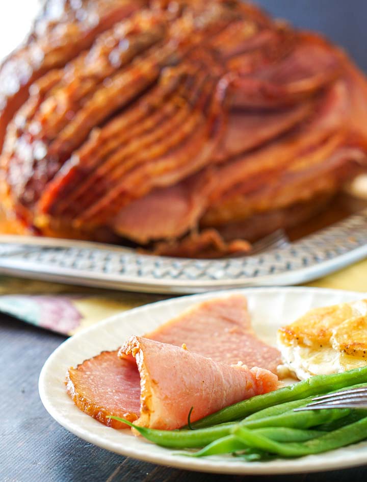 white plate with a slice of ham and green beans with a spiral sugar free glazed ham in the background