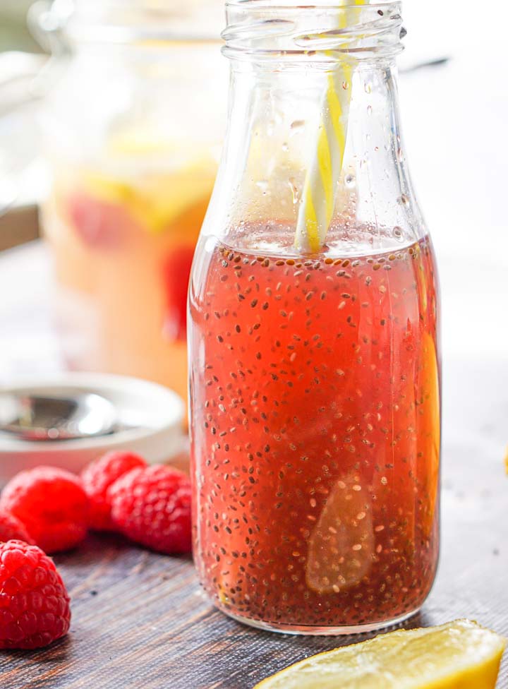jar of low carb raspberry lemonade chia drink with a yellow striped straw and with fresh raspberries