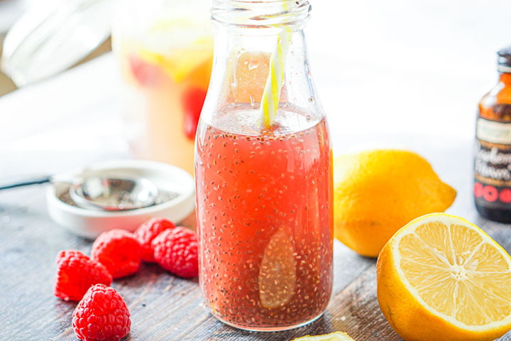jar of raspberry lemonade chia drink with a yellow striped straw and with fresh lemons and raspberries surrounding it