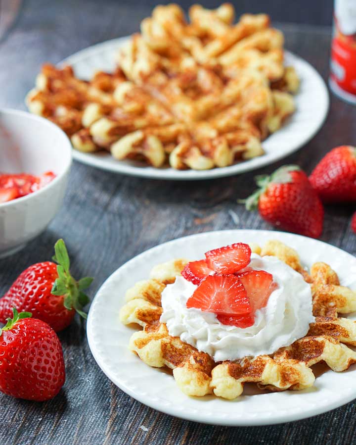 white plate with low carb waffle with fresh strawberries and whipped cream and waffles in the background