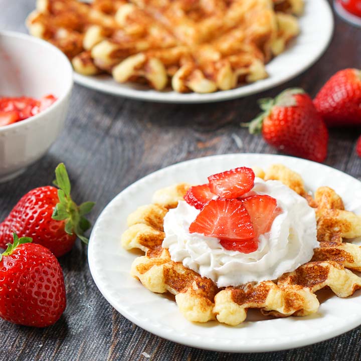 white plate with keto chaffle with fresh strawberries and whipped cream and waffles in the background